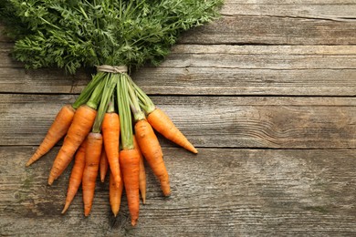 Photo of Bunch of tasty ripe juicy carrots on wooden table, top view. Space for text