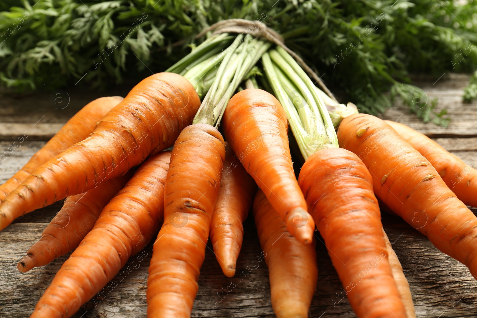 Photo of Bunch of tasty ripe juicy carrots on wooden table, closeup