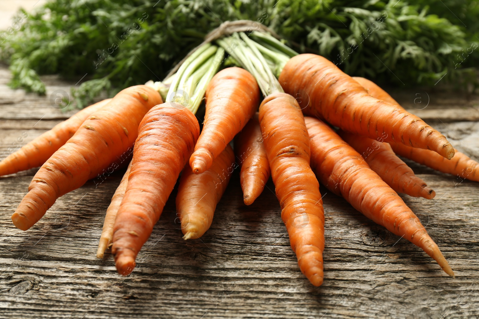 Photo of Bunch of tasty ripe juicy carrots on wooden table, closeup