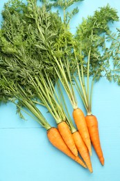 Photo of Tasty ripe juicy carrots on light blue wooden table, flat lay