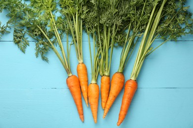 Photo of Tasty ripe juicy carrots on light blue wooden table, flat lay