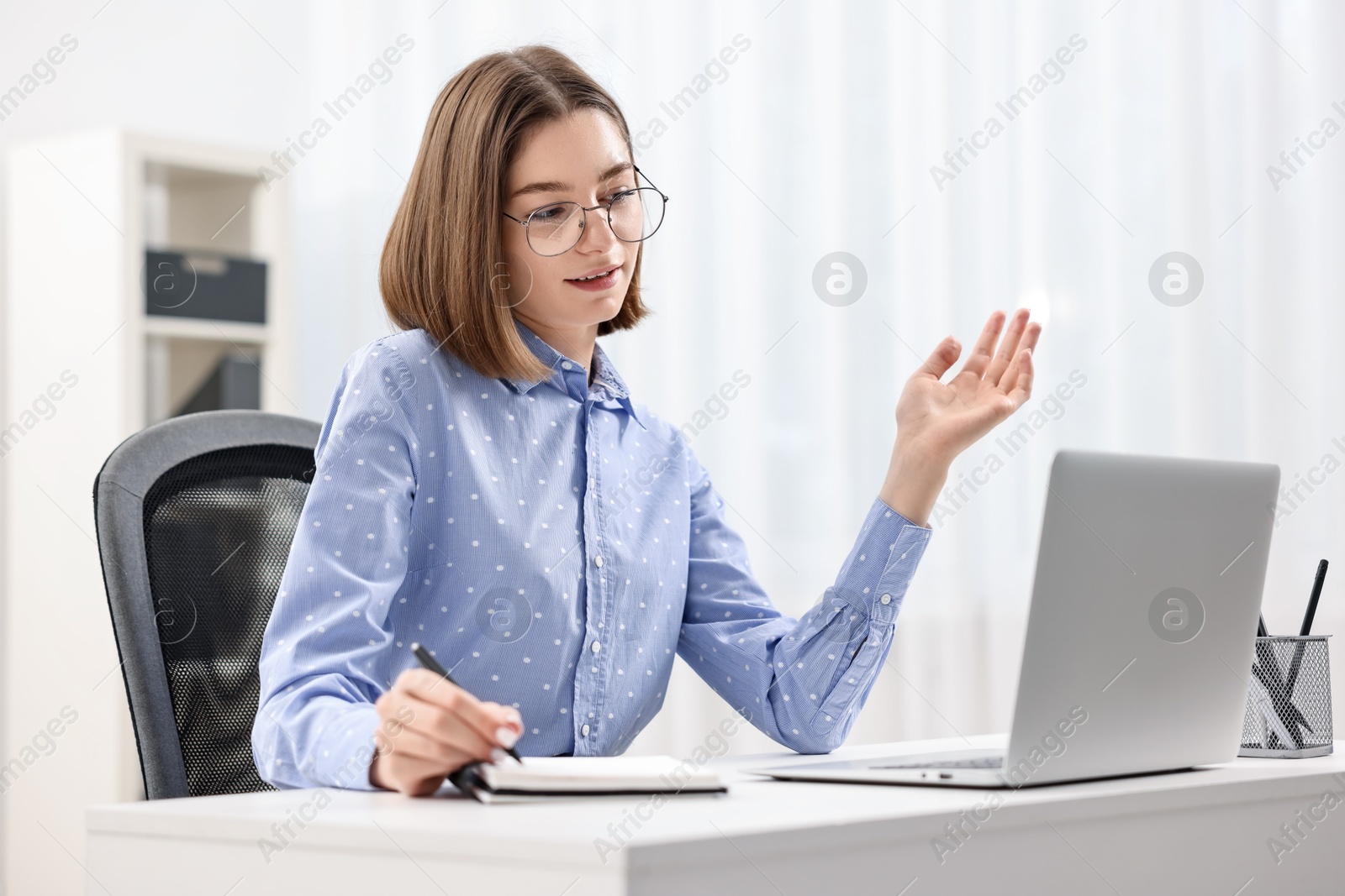 Photo of Teenager taking notes while working with laptop at home. Remote job