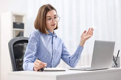 Teenager taking notes while working with laptop at home. Remote job