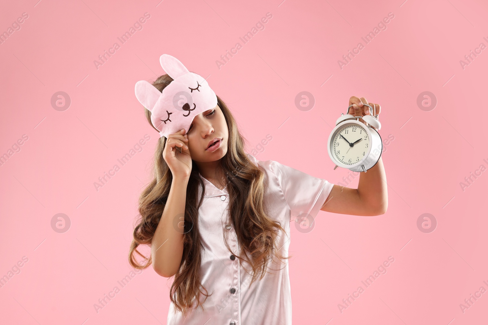 Photo of Overslept girl with sleep mask and alarm clock on pink background