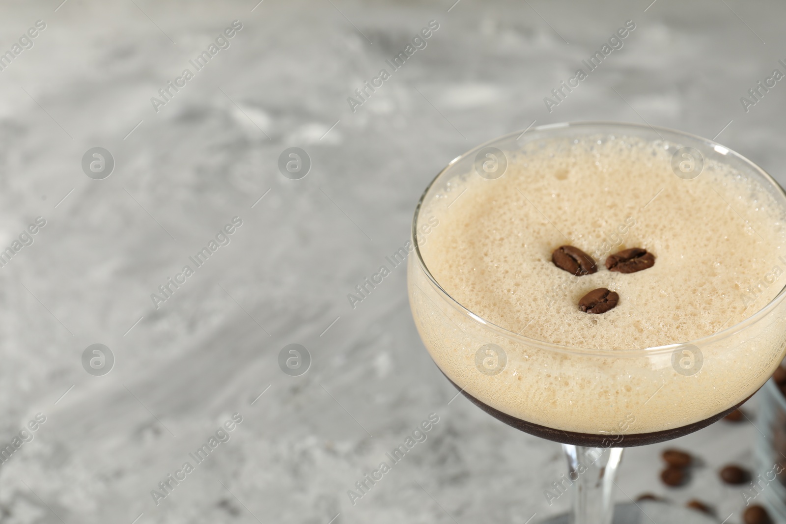 Photo of Glass of fresh coffee cocktail on gray textured table, closeup. Space for text