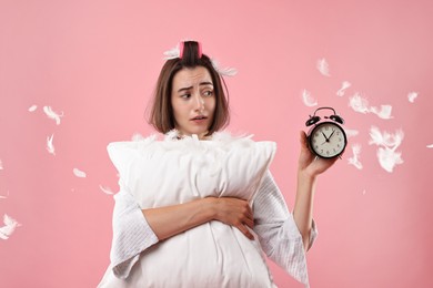 Photo of Overslept young woman with pillow and alarm clock on pink background