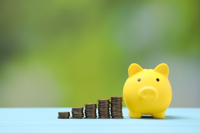 Yellow piggy bank and stacks of coins on light blue table against blurred background