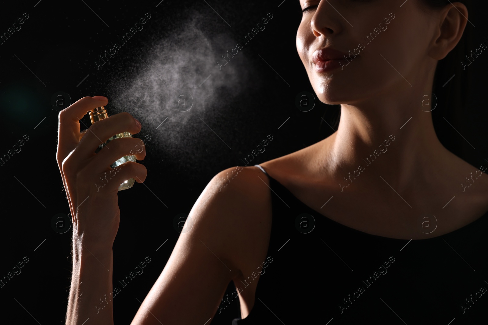 Photo of Woman spraying perfume on black background, closeup