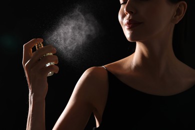 Woman spraying perfume on black background, closeup