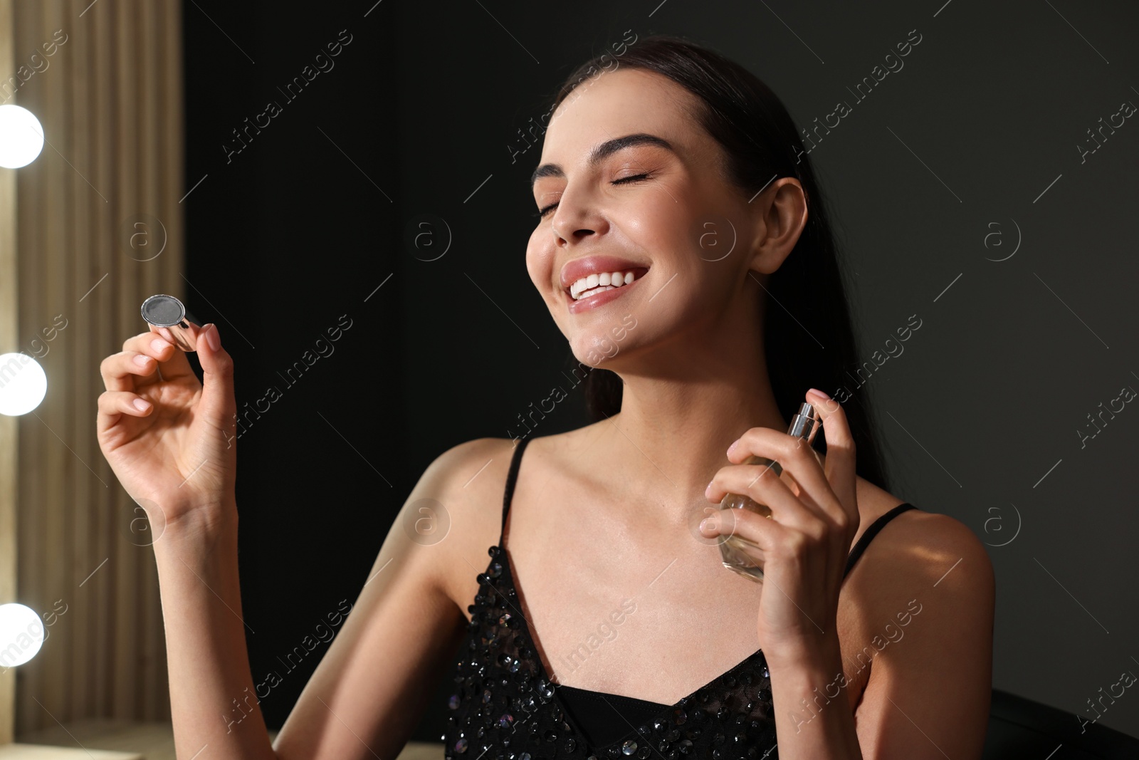 Photo of Smiling woman spraying perfume in makeup room