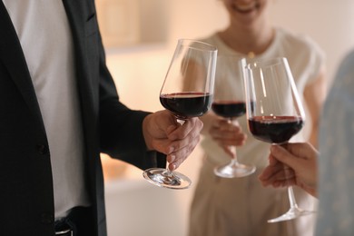 Friends with glasses of red wine indoors, selective focus