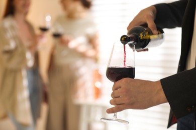 Man pouring red wine into glass indoors, selective focus