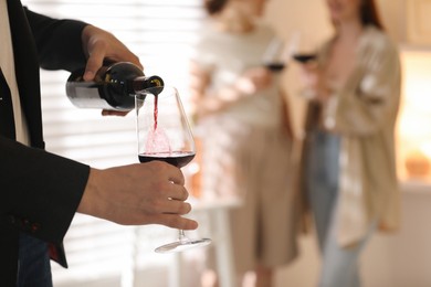 Man pouring red wine into glass indoors, selective focus