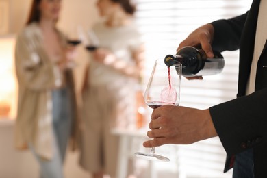 Man pouring red wine into glass indoors, selective focus