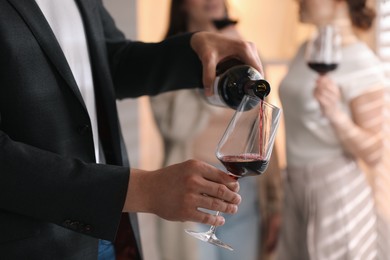 Photo of Man pouring red wine into glass indoors, selective focus