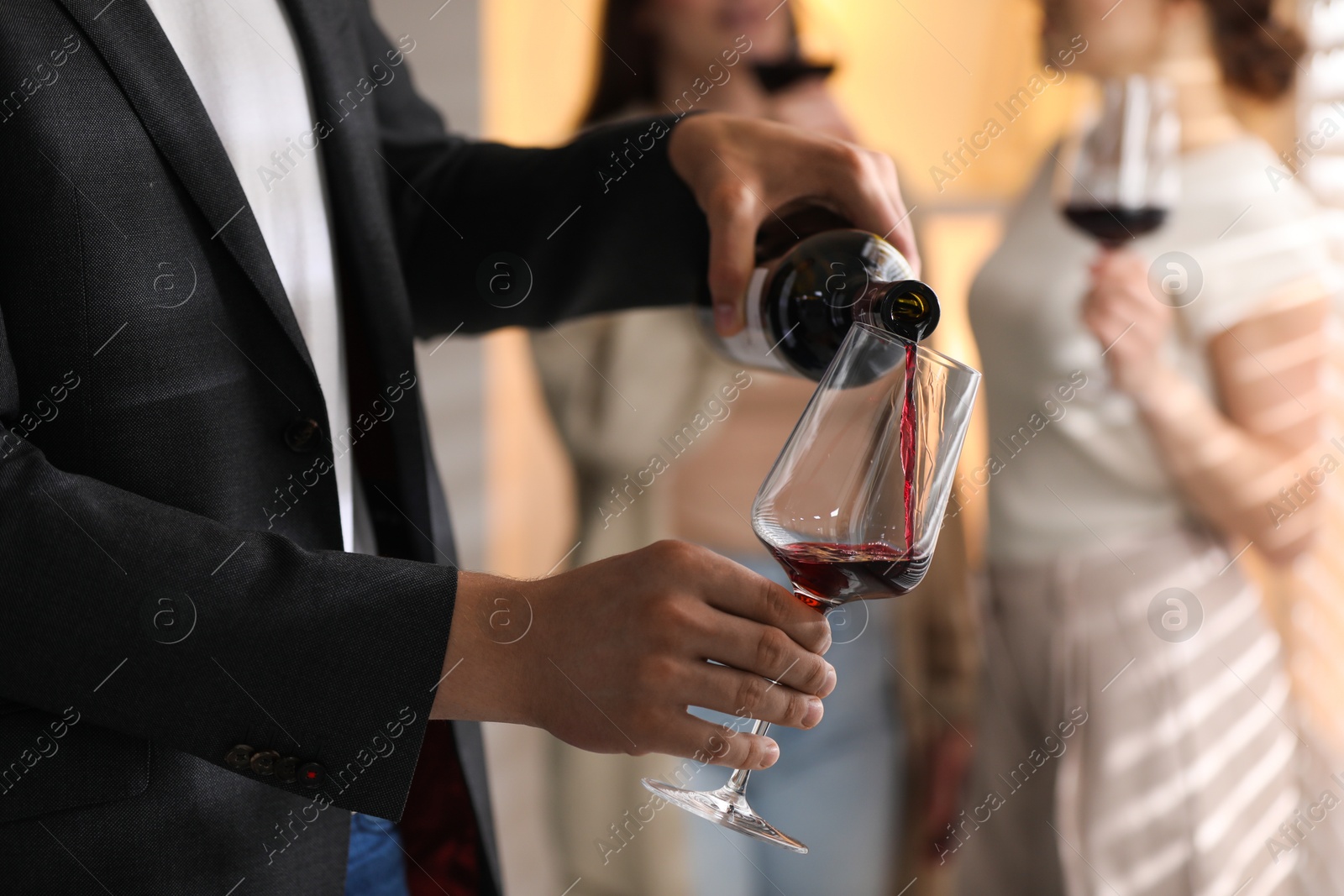 Photo of Man pouring red wine into glass indoors, selective focus