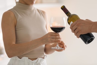 Photo of Man pouring red wine into woman`s glass indoors, closeup