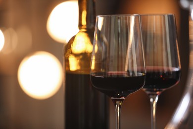 Photo of Tasty wine in glass and bottle against blurred lights, closeup