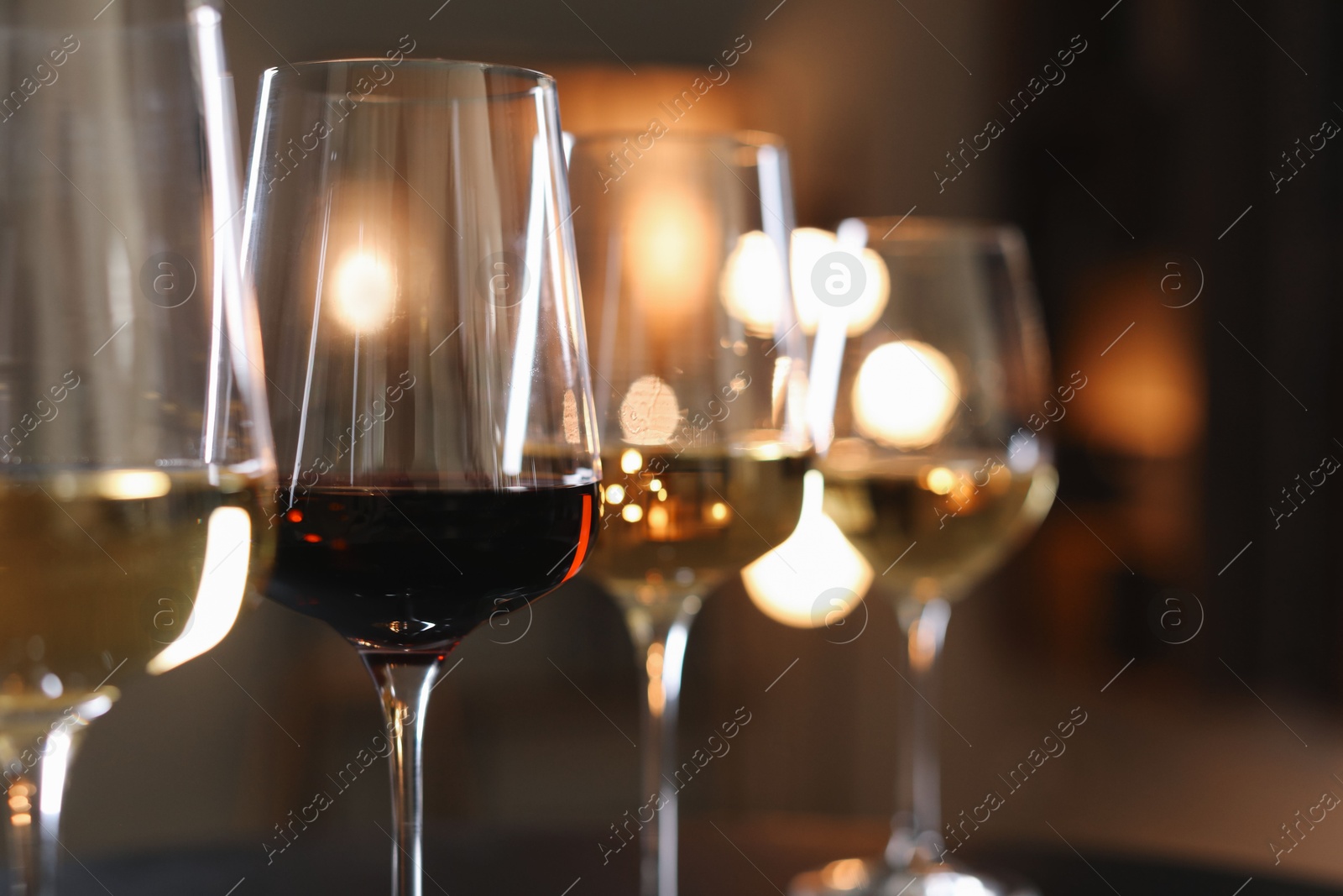 Photo of Different tasty wines in glasses against blurred lights, closeup