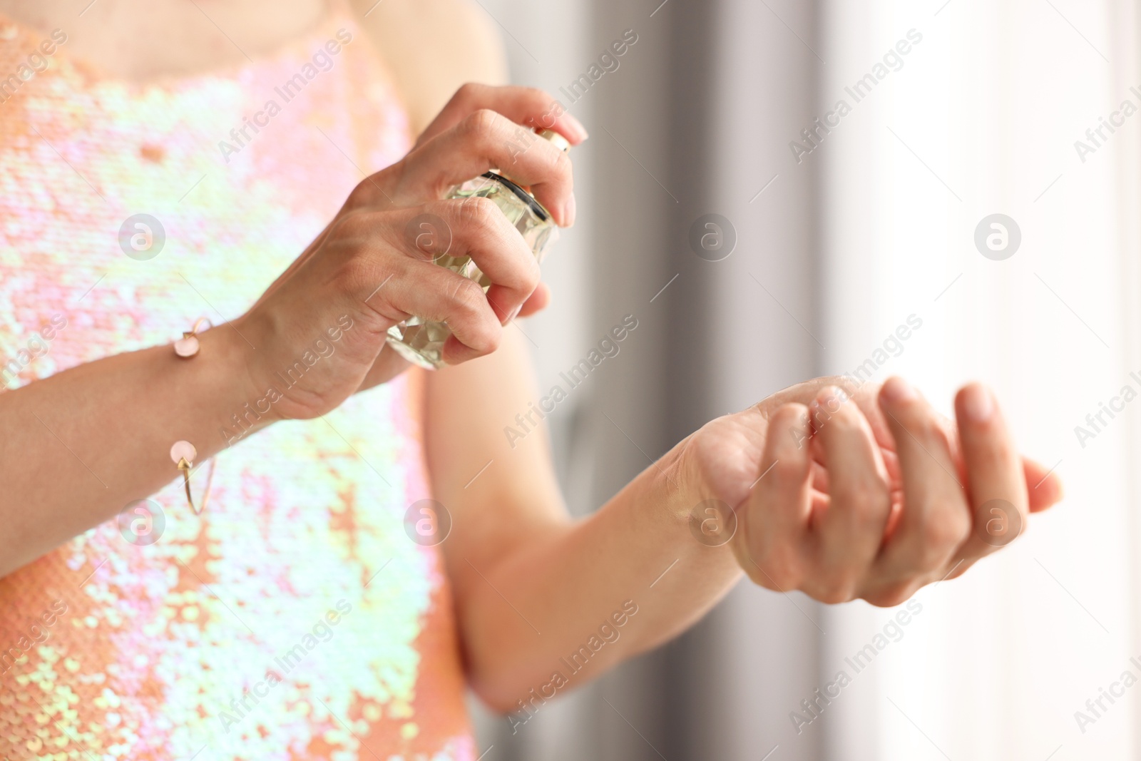 Photo of Woman spraying perfume onto wrist indoors, closeup