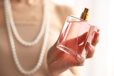 Woman with bottle of perfume on blurred background, closeup