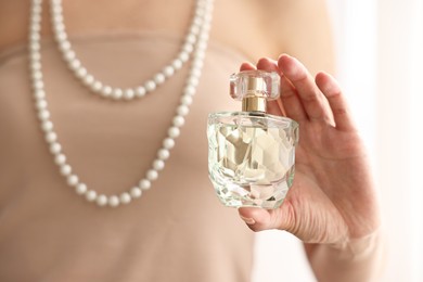 Woman with bottle of perfume on blurred background, closeup