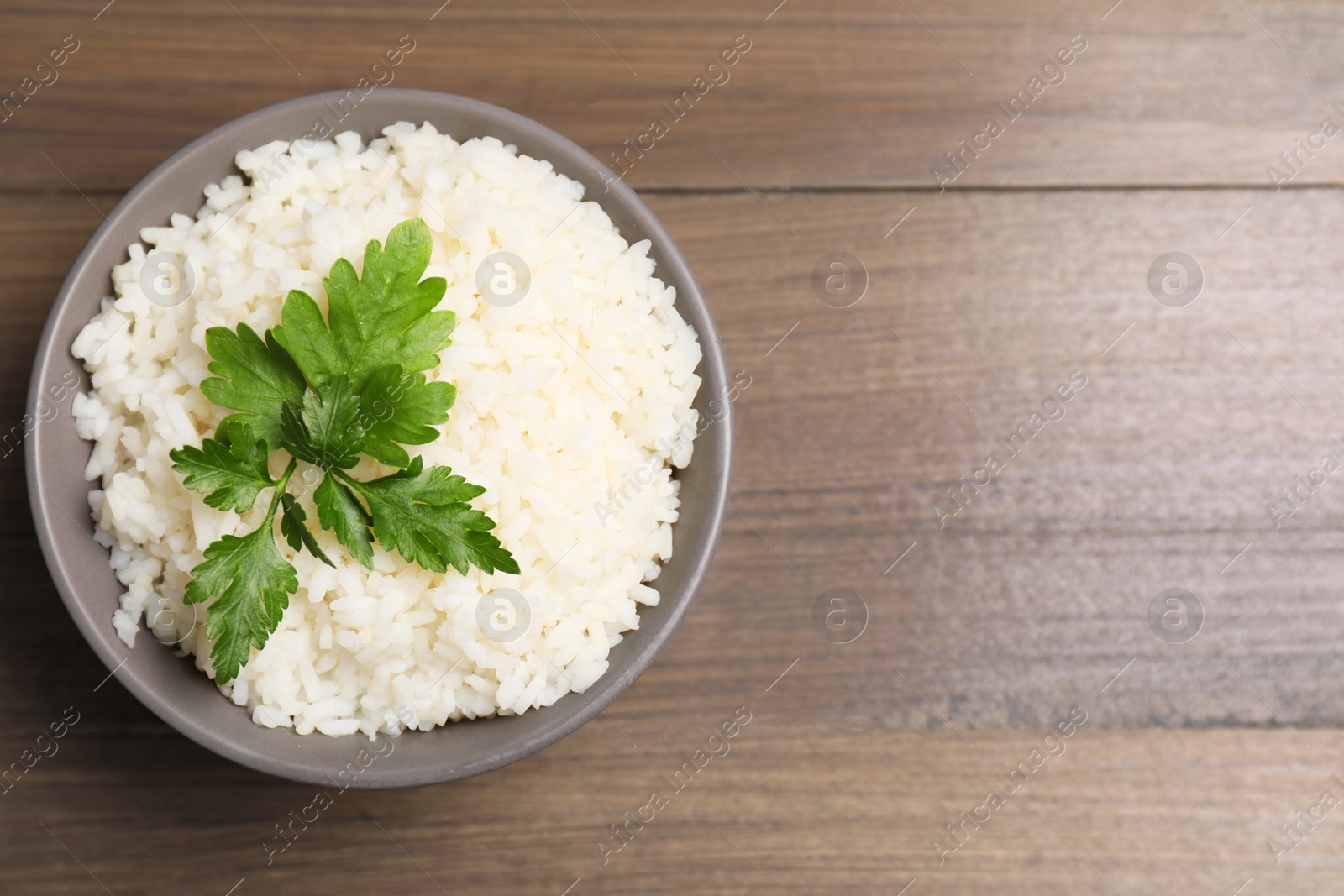 Photo of Bowl of delicious boiled rice with parsley on wooden table, top view. Space for text