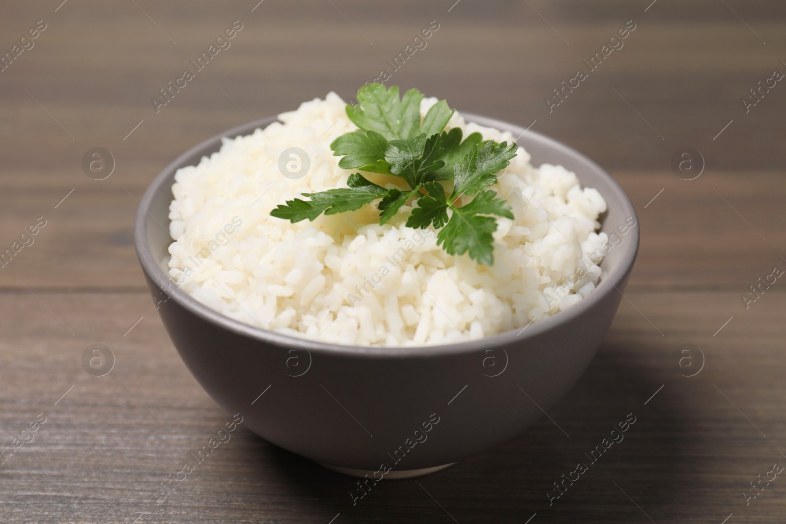 Photo of Bowl of delicious boiled rice with parsley on wooden table, closeup