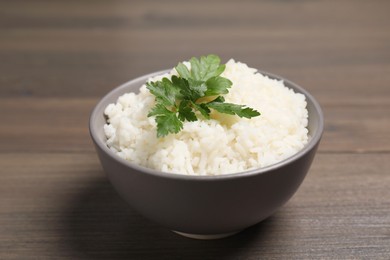 Bowl of delicious boiled rice with parsley on wooden table, closeup