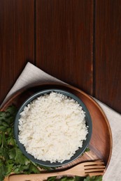 Delicious boiled rice served with parsley on wooden table, top view. Space for text