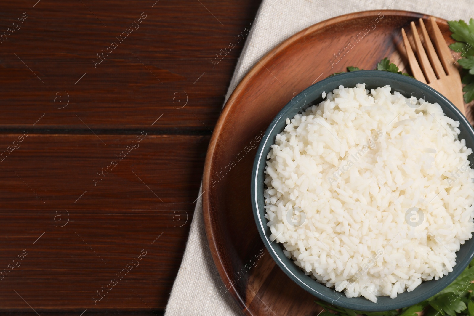 Photo of Delicious boiled rice served with parsley on wooden table, top view. Space for text