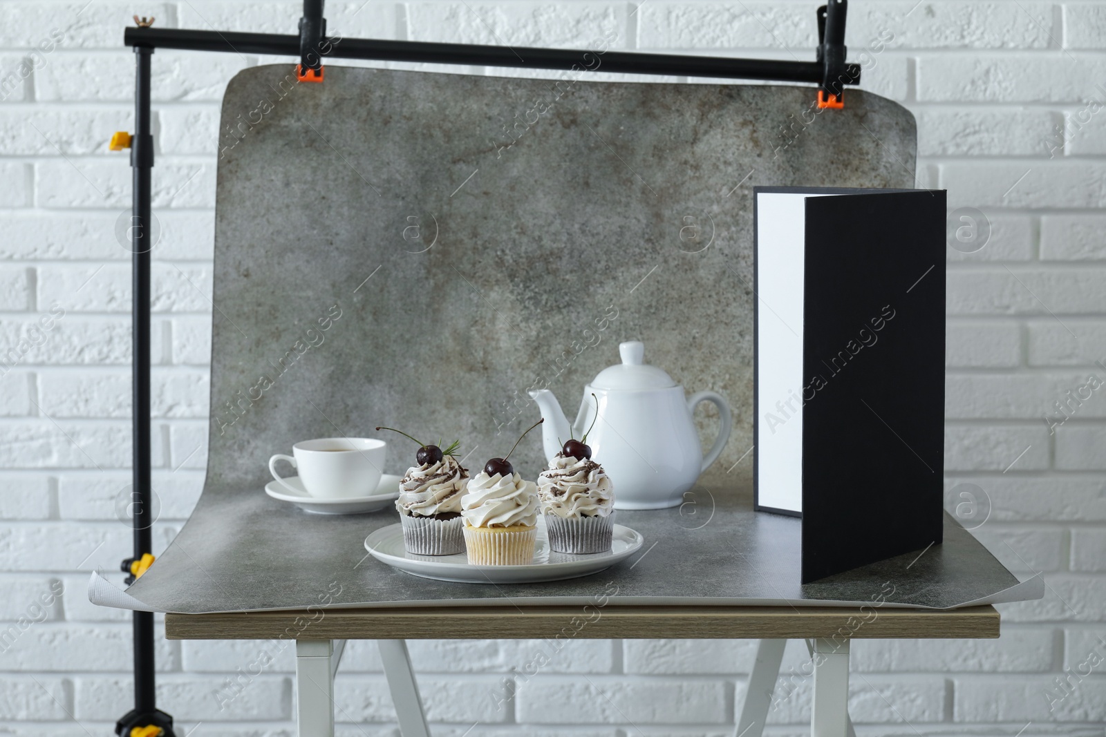 Photo of Cupcakes, tea and light reflector on table in studio. Professional food photography