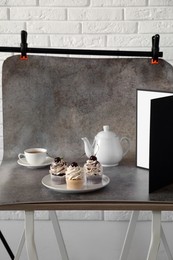 Photo of Cupcakes, tea and light reflector on table in studio. Professional food photography