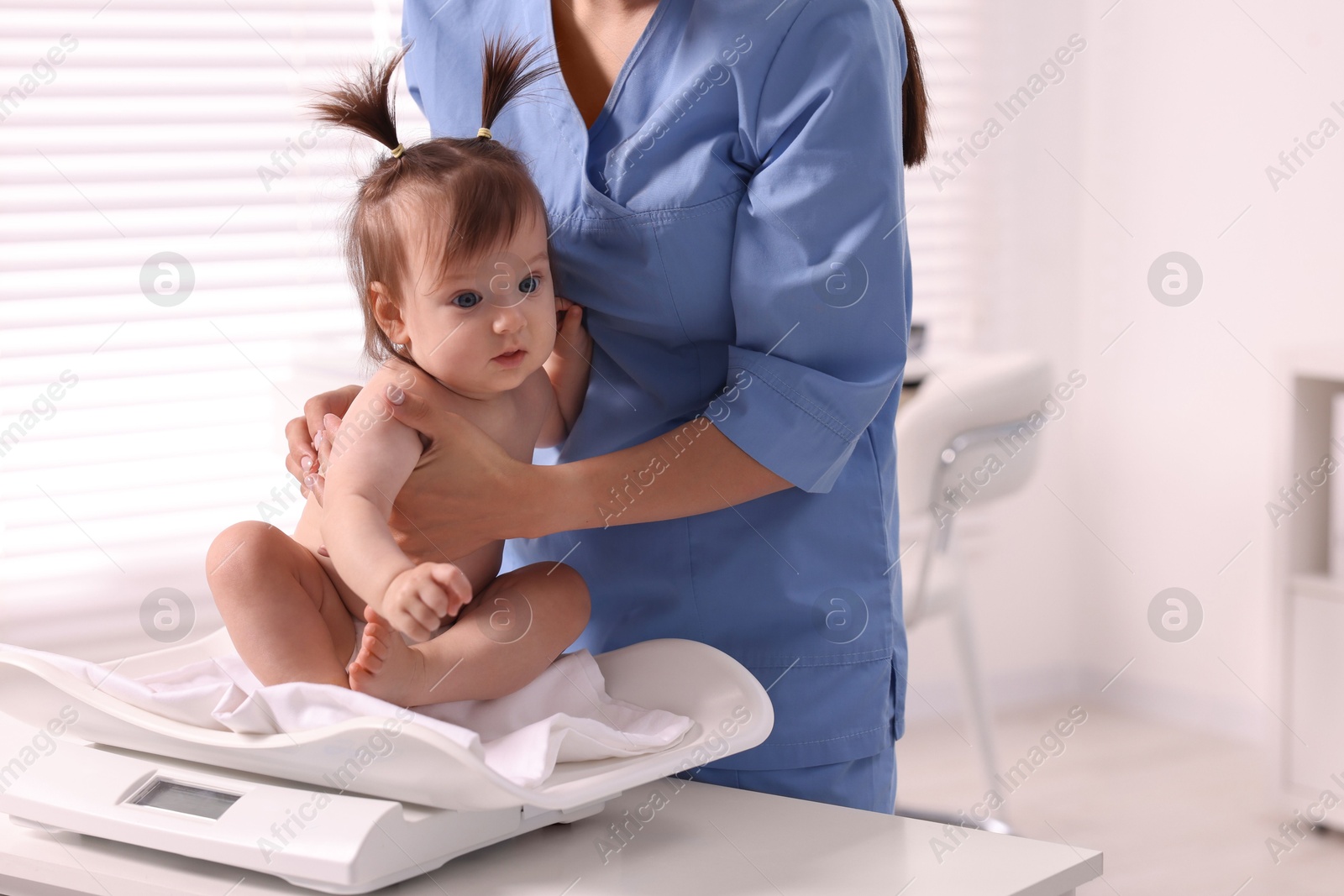 Photo of Pediatrician weighting cute little girl in clinic. Checking baby's health