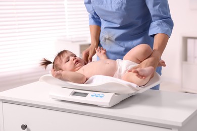 Photo of Pediatrician weighting cute little girl in clinic, closeup. Checking baby's health