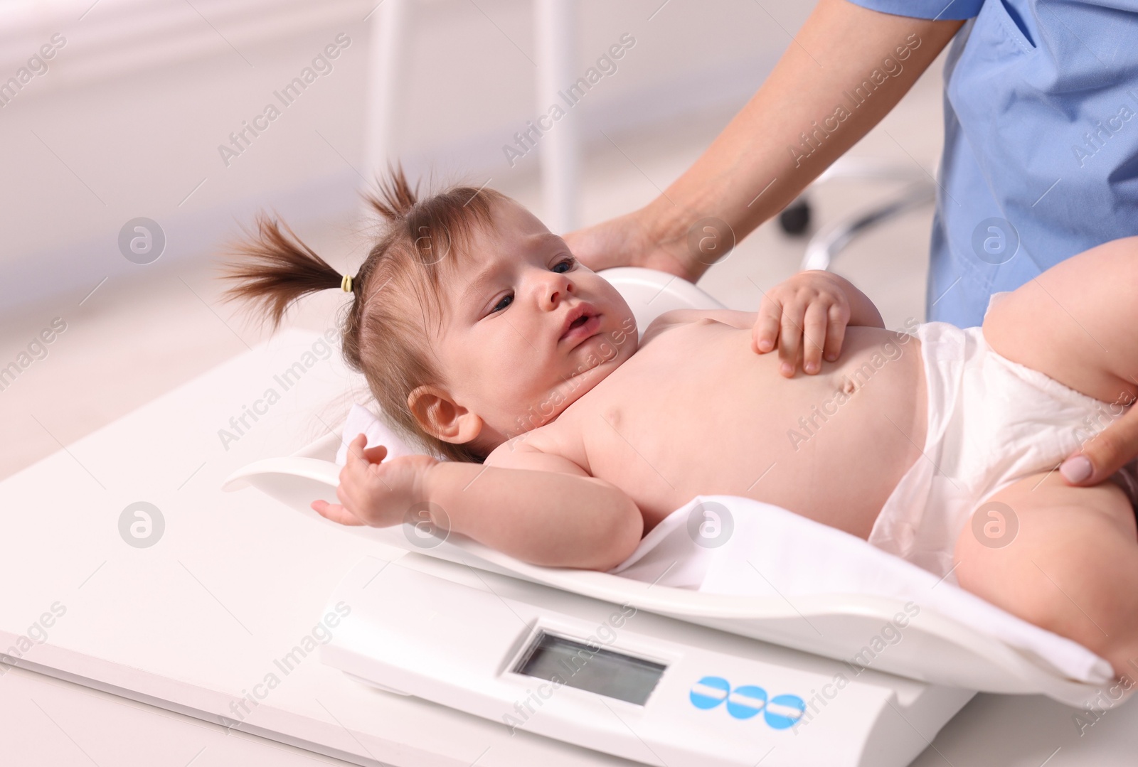 Photo of Pediatrician weighting cute little girl in clinic, closeup. Checking baby's health