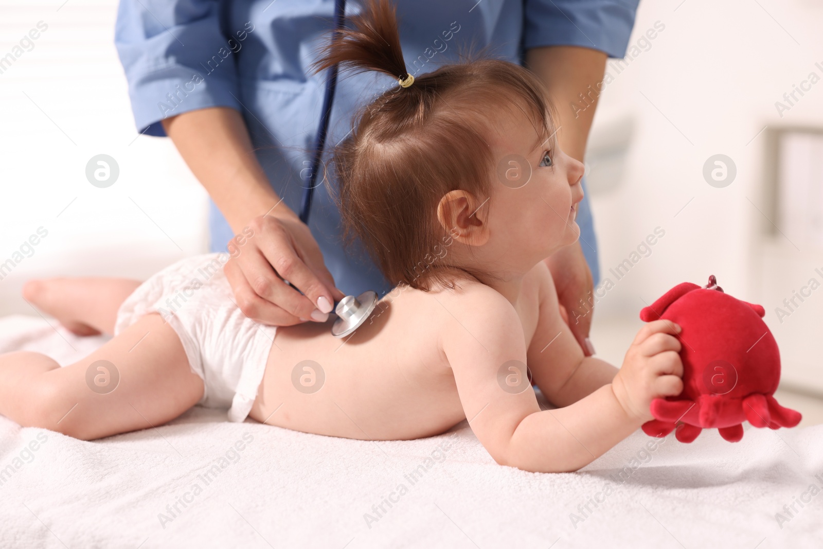 Photo of Pediatrician examining cute little girl with stethoscope in clinic, closeup. Checking baby's health