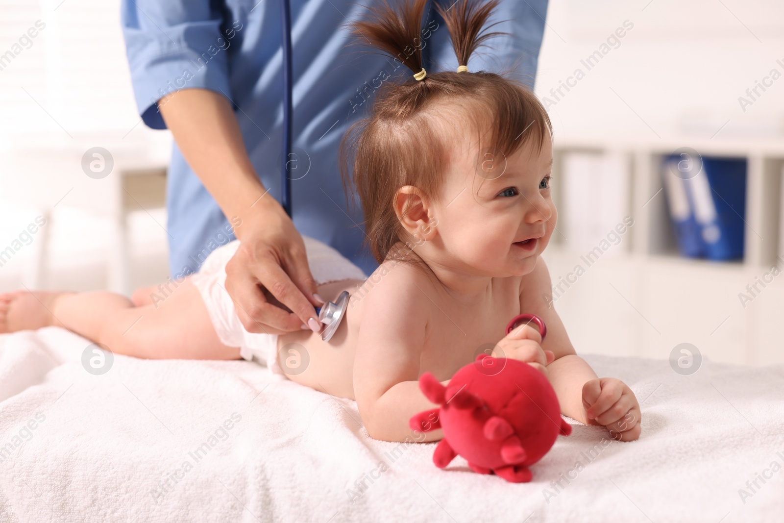 Photo of Pediatrician examining cute little girl with stethoscope in clinic, closeup. Checking baby's health