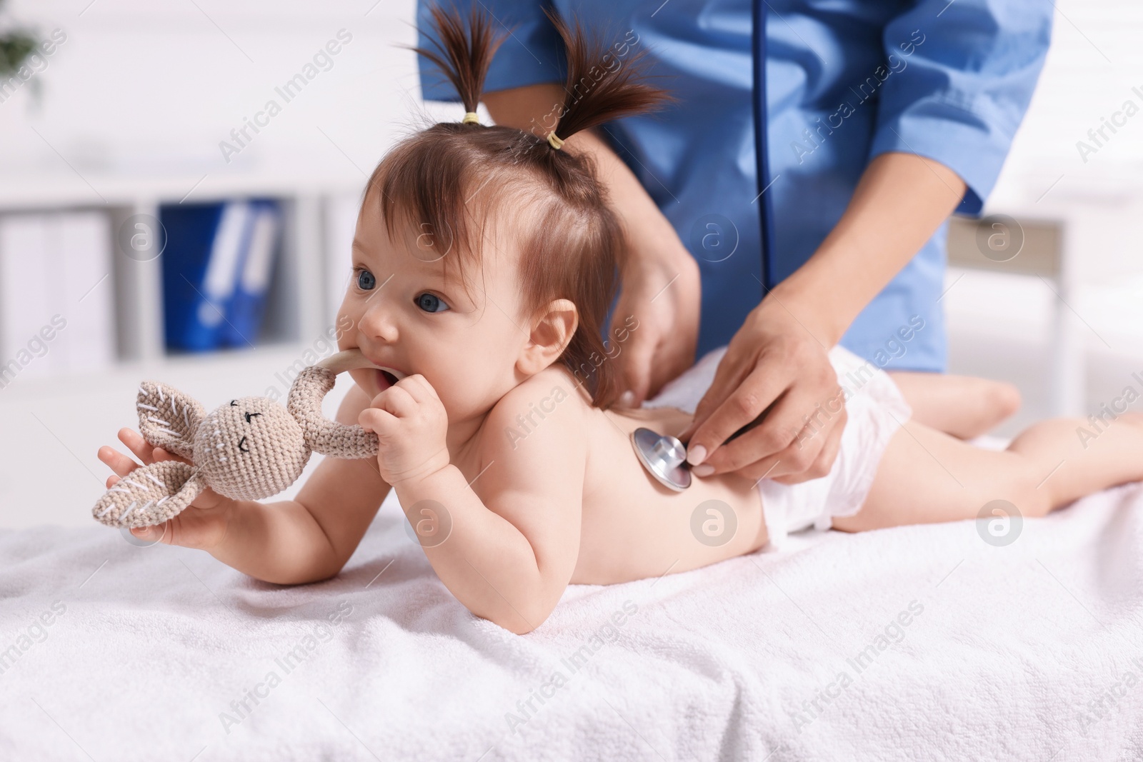 Photo of Pediatrician examining cute little girl with stethoscope in clinic, closeup. Checking baby's health