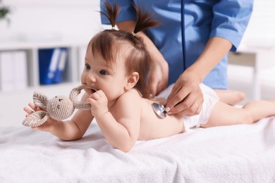 Photo of Pediatrician examining cute little girl with stethoscope in clinic, closeup. Checking baby's health