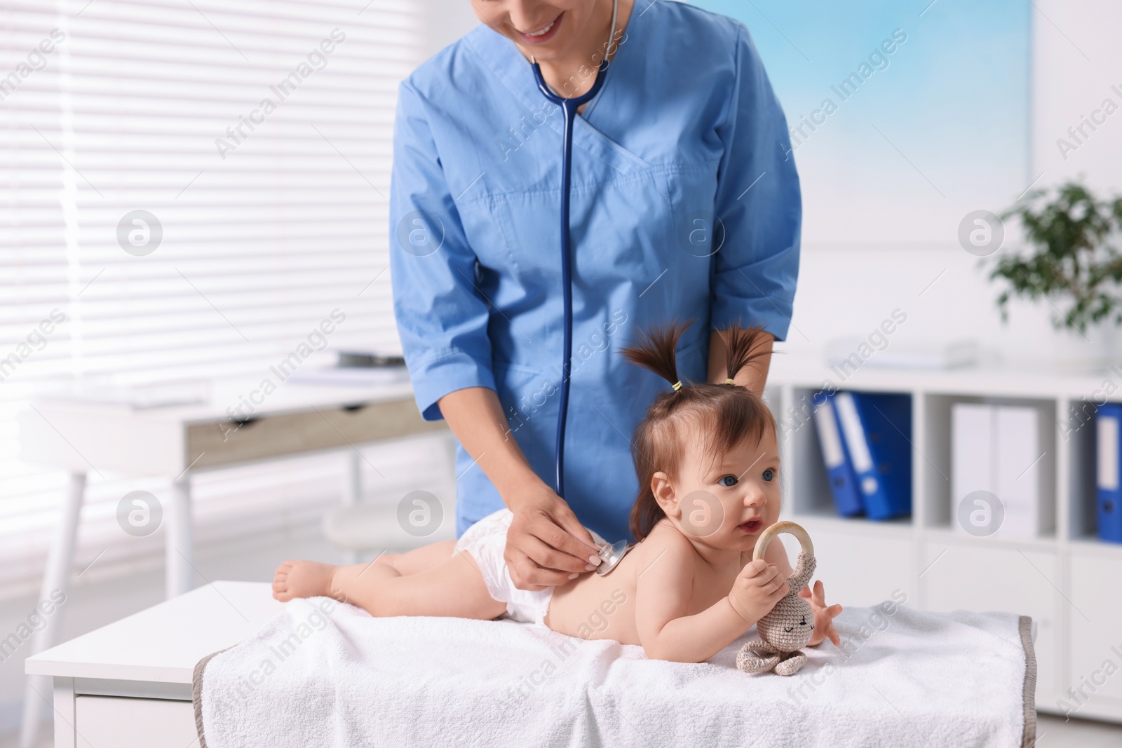 Photo of Pediatrician examining cute little girl with stethoscope in clinic, closeup. Checking baby's health