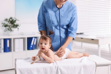 Photo of Pediatrician examining cute little girl with stethoscope in clinic, closeup. Checking baby's health