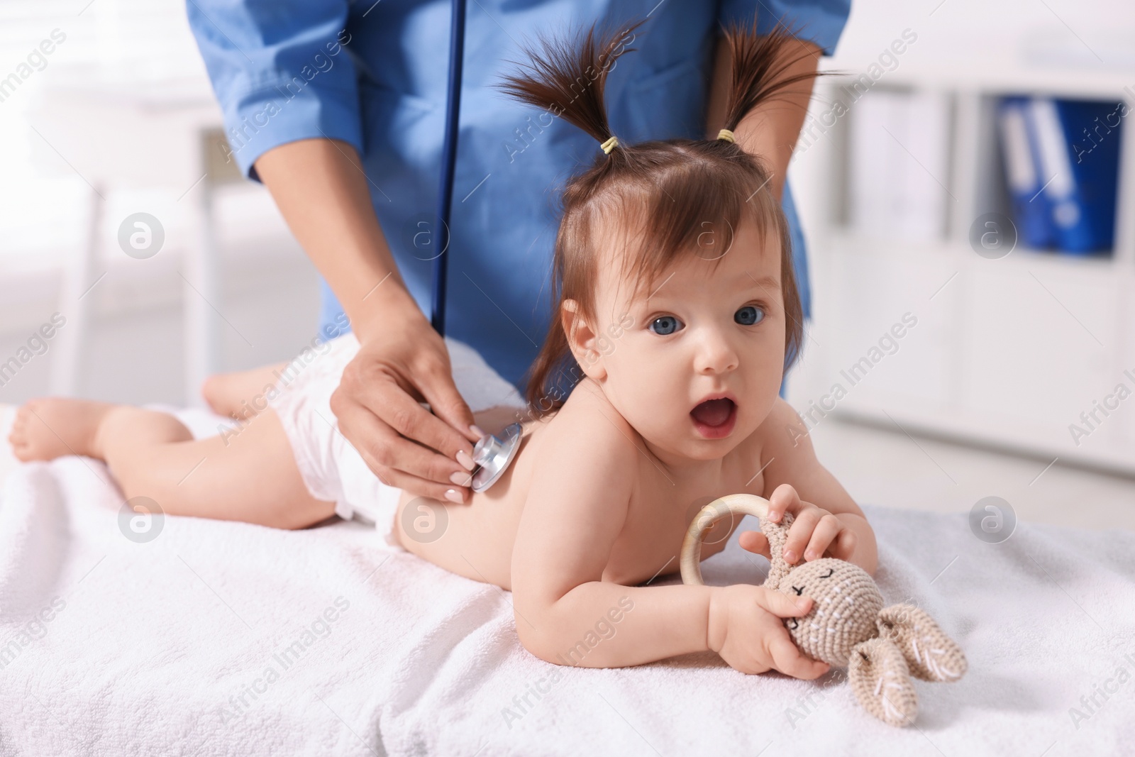 Photo of Pediatrician examining cute little girl with stethoscope in clinic, closeup. Checking baby's health