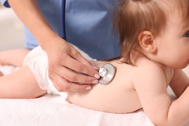 Photo of Pediatrician examining cute little girl with stethoscope in clinic, closeup. Checking baby's health