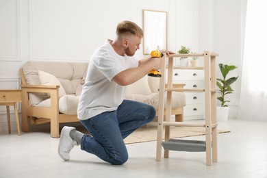 Man with electric screwdriver assembling furniture in room