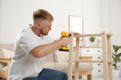 Man with electric screwdriver assembling furniture in room