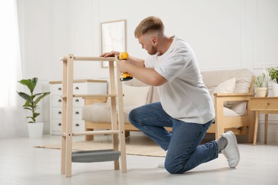 Photo of Man with electric screwdriver assembling furniture in room