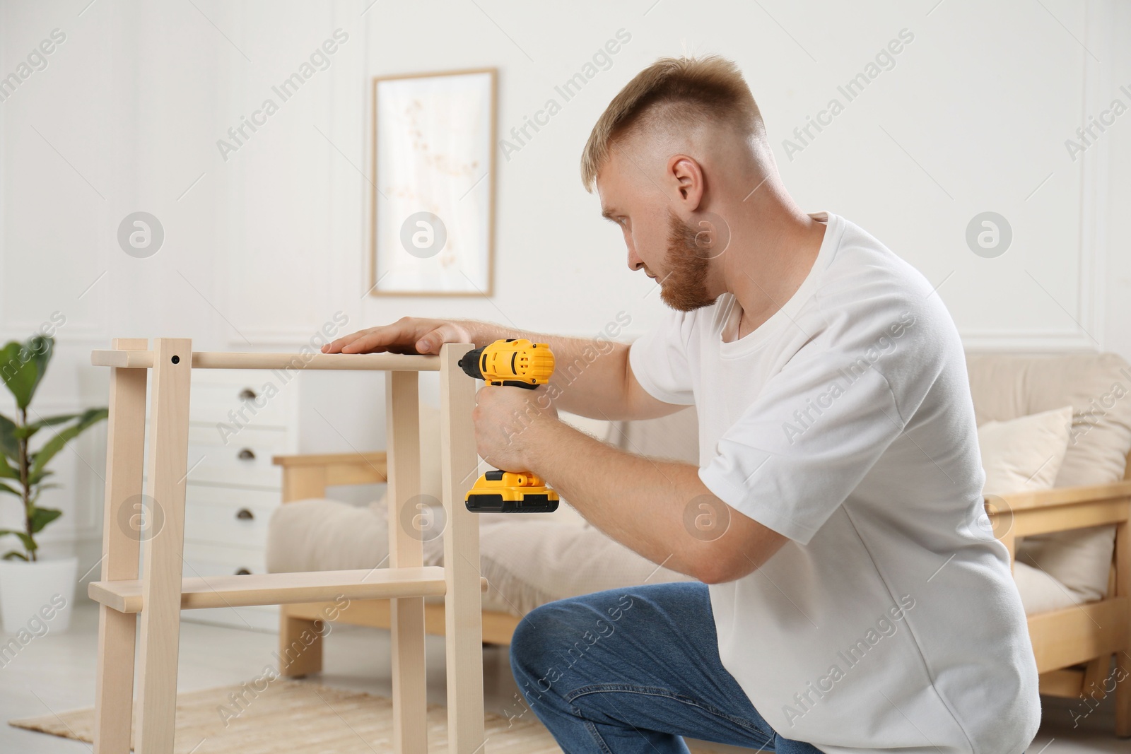 Photo of Man with electric screwdriver assembling furniture in room