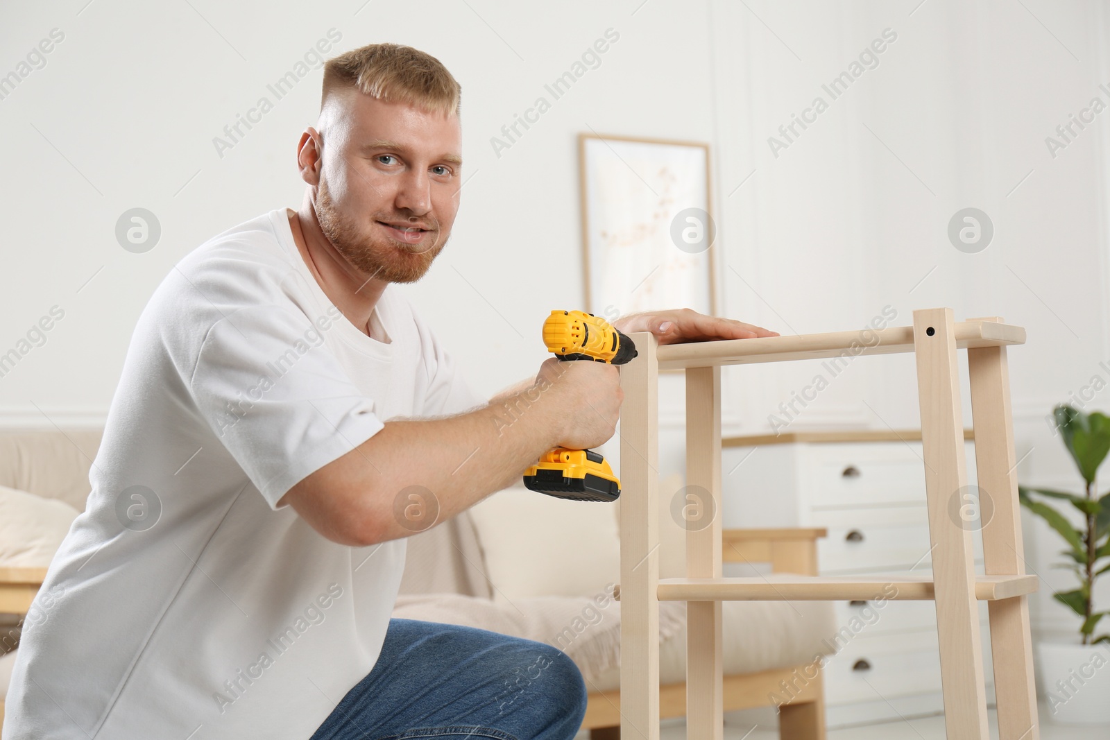 Photo of Man with electric screwdriver assembling furniture in room