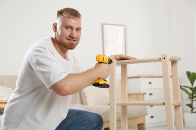 Photo of Man with electric screwdriver assembling furniture in room